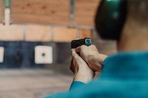 un' uomo pratiche tiro un' pistola nel un' tiro gamma mentre indossare protettivo cuffie foto