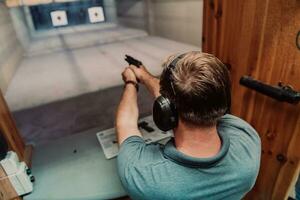 un' uomo pratiche tiro un' pistola nel un' tiro gamma mentre indossare protettivo cuffie foto