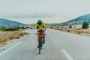 pieno lunghezza ritratto di un attivo triatleta nel abbigliamento sportivo e con un' protettivo casco equitazione un' bicicletta. selettivo messa a fuoco foto