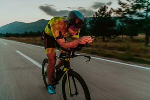 notte viaggio. pieno lunghezza ritratto di un attivo triatleta nel abbigliamento sportivo e con un' protettivo casco equitazione un' bicicletta nel notte tempo.. selettivo messa a fuoco foto