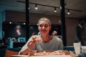 un' moderno bionda mangiare Pizza nel sua ufficio su un' rompere a partire dal opera foto