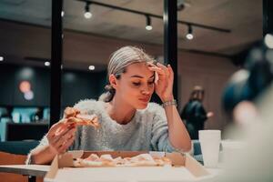 un' moderno bionda mangiare Pizza nel sua ufficio su un' rompere a partire dal opera foto