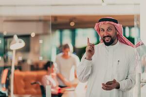 mezzo orientale arabo uomo d'affari nel il ufficio A proposito di su smartphone nel davanti di il suo squadra foto