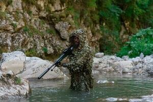 un' militare uomo o softair giocatore nel un' camuffare completo da uomo Sneaking il fiume e obiettivi a partire dal un' cecchino fucile per il lato o per obbiettivo. foto
