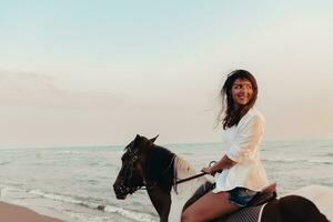 donna nel estate Abiti gode equitazione un' cavallo su un' bellissimo sabbioso spiaggia a tramonto. selettivo messa a fuoco foto