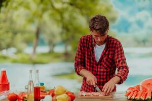 un' uomo preparazione un' delizioso cena per il suo amici chi siamo avendo divertimento di il fiume nel natura foto