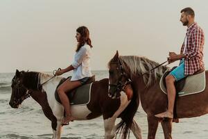 un' amorevole coppia nel estate Abiti equitazione un' cavallo su un' sabbioso spiaggia a tramonto. mare e tramonto nel il sfondo. selettivo messa a fuoco foto