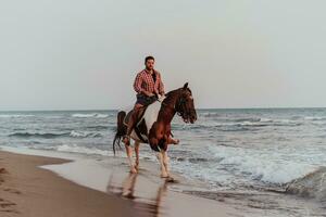 un' moderno uomo nel estate Abiti gode equitazione un' cavallo su un' bellissimo sabbioso spiaggia a tramonto. selettivo messa a fuoco foto