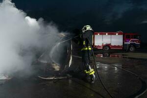 i vigili del fuoco utilizzando acqua fuoco estintore per combattente con il fuoco fiamma nel auto incidente. pompiere industriale e pubblico sicurezza concetto salvare nel notte. foto