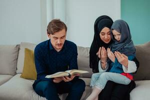 contento musulmano famiglia godendo il santo mese di Ramadan mentre preghiere e lettura il Corano insieme nel un' moderno casa foto