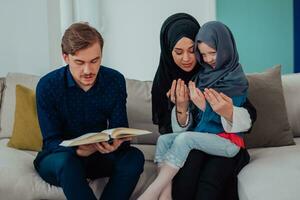 contento musulmano famiglia godendo il santo mese di Ramadan mentre preghiere e lettura il Corano insieme nel un' moderno casa foto