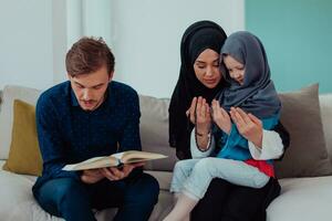 contento musulmano famiglia godendo il santo mese di Ramadan mentre preghiere e lettura il Corano insieme nel un' moderno casa foto