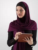 bellissimo e moderno giovane Arabo donna d'affari nel hijab utilizzando un' tavoletta computer mentre in posa su leggero sfondo e sorridente a il telecamera. attività commerciale diversità concetto, musulmano signora. foto