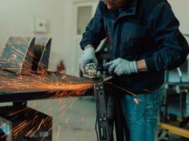 interno di una fabbrica di ingegneria dell'industria pesante con un lavoratore industriale che utilizza una smerigliatrice angolare e taglia un tubo di metallo. appaltatore in uniforme di sicurezza e elmetto per la produzione di strutture metalliche. foto