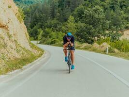 pieno lunghezza ritratto di un attivo triatleta nel abbigliamento sportivo e con un' protettivo casco equitazione un' bicicletta. selettivo messa a fuoco foto