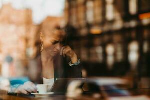 donna nel un' caffè negozio bevanda caffè visto attraverso bicchiere con riflessi come essi sedersi a un' tavolo chat e ridendo foto