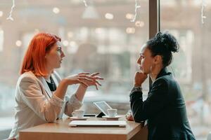 Due giovane attività commerciale donne seduta a tavolo nel bar. ragazza Spettacoli collega informazione su il computer portatile schermo. ragazza utilizzando smartphone, blogging. lavoro di squadra, attività commerciale incontro. foto