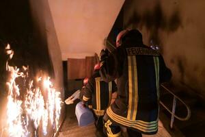 coraggioso vigile del fuoco discende le scale di un' ardente edificio e detiene salvato ragazza nel il suo braccia. Aperto fuoco e uno pompiere nel il sfondo. foto