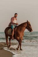 un' moderno uomo nel estate Abiti gode equitazione un' cavallo su un' bellissimo sabbioso spiaggia a tramonto. selettivo messa a fuoco foto