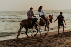 un' amorevole coppia nel estate Abiti equitazione un' cavallo su un' sabbioso spiaggia a tramonto. mare e tramonto nel il sfondo. selettivo messa a fuoco foto