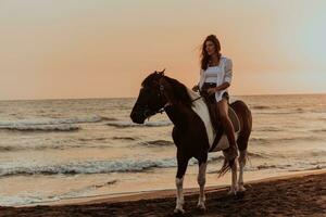 donna nel estate Abiti gode equitazione un' cavallo su un' bellissimo sabbioso spiaggia a tramonto. selettivo messa a fuoco foto