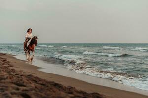 donna nel estate Abiti gode equitazione un' cavallo su un' bellissimo sabbioso spiaggia a tramonto. selettivo messa a fuoco foto