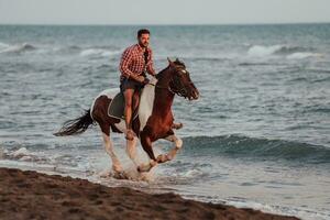 un' moderno uomo nel estate Abiti gode equitazione un' cavallo su un' bellissimo sabbioso spiaggia a tramonto. selettivo messa a fuoco foto