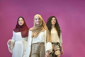 tre musulmano donne nel hijab nel un' moderno Abiti posa contro un' rosa sfondo foto