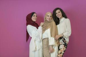 gruppo di bellissimo musulmano donne Due di loro nel alla moda vestito con hijab utilizzando mobile Telefono isolato su rosa sfondo che rappresentano moderno Islam moda tecnologia e Ramadan kareem concetto foto