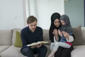 tradizionale musulmano famiglia genitori con bambini lettura Corano e preghiere insieme su il divano prima iftar cena durante un' Ramadan festa a casa foto