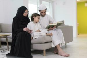 tradizionale musulmano famiglia genitori con bambini lettura Corano e preghiere insieme su il divano prima iftar cena durante un' Ramadan festa a casa foto