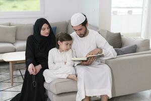 tradizionale musulmano famiglia genitori con bambini lettura Corano e preghiere insieme su il divano prima iftar cena durante un' Ramadan festa a casa foto