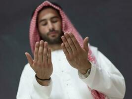 un' giovane arabo uomo nel tradizionale Abiti fabbricazione un' tradizionale preghiera per Dio mantiene il suo mani nel preghiere gesto nel davanti di un' nero sfondo foto