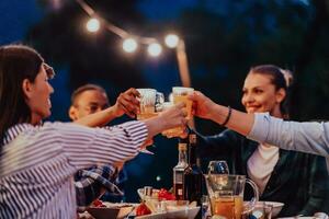 un' gruppo di giovane diverso persone avendo cena su il terrazza di un' moderno Casa nel il sera. divertimento per amici e famiglia. celebrazione di vacanze, matrimoni con barbecue. foto