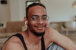 testa tiro di africano americano uomo indossare bicchieri e cuffie seduta su vivente camera pavimento foto