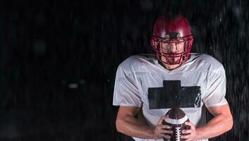 americano calcio campo solitario atleta guerriero in piedi su un' campo detiene il suo casco e pronto per giocare a. giocatore preparazione per correre, attacco e Punto touchdown. piovoso notte con drammatico nebbia, blu leggero foto