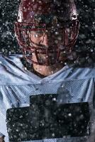 americano calcio campo solitario atleta guerriero in piedi su un' campo detiene il suo casco e pronto per giocare a. giocatore preparazione per correre, attacco e Punto touchdown. piovoso notte con drammatico nebbia, blu leggero foto