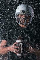 americano calcio campo solitario atleta guerriero in piedi su un' campo detiene il suo casco e pronto per giocare a. giocatore preparazione per correre, attacco e Punto touchdown. piovoso notte con drammatico nebbia, blu leggero foto