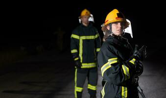 i vigili del fuoco utilizzando un' acqua tubo flessibile per eliminare un' fuoco rischio. squadra di femmina e maschio pompiere nel pericoloso salvare missione. foto