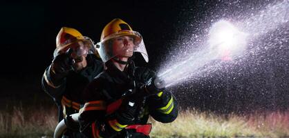 i vigili del fuoco utilizzando un' acqua tubo flessibile per eliminare un' fuoco rischio. squadra di femmina e maschio pompiere nel pericoloso salvare missione. foto