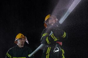 i vigili del fuoco utilizzando un' acqua tubo flessibile per eliminare un' fuoco rischio. squadra di femmina e maschio pompiere nel pericoloso salvare missione. foto