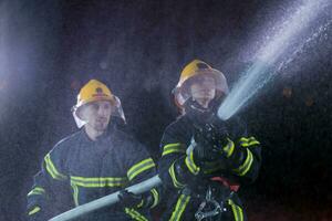 i vigili del fuoco utilizzando un' acqua tubo flessibile per eliminare un' fuoco rischio. squadra di femmina e maschio pompiere nel pericoloso salvare missione. foto