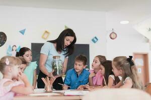 femmina insegnante con bambini nel biologia classe a elementare scuola conduzione biologia o botanico scientifico sperimentare di sostenibile in crescita impianti. apprendimento di impianti nel un' bicchiere vaso foto