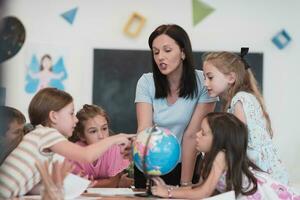 femmina insegnante con bambini nel geografia classe guardare a globo. lato Visualizza di gruppo di diverso contento scuola bambini con globo nel aula a scuola. foto