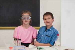 elementare scuola scienza aula entusiasta insegnante spiega chimica per diverso gruppo di figli, poco ragazzo miscele sostanze chimiche nel bicchieri. bambini imparare con interesse foto