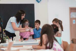 elementare scuola scienza aula entusiasta insegnante spiega chimica per diverso gruppo di figli, poco ragazzo miscele sostanze chimiche nel bicchieri. bambini imparare con interesse foto