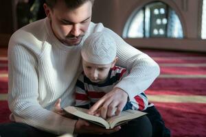 musulmano preghiera padre e figlio nel moschea preghiere e lettura agrifoglio libro Corano insieme islamico formazione scolastica concetto foto