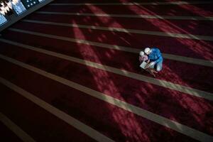 musulmano preghiera padre e figlio nel moschea preghiere e lettura agrifoglio libro Corano insieme islamico formazione scolastica concetto foto