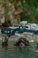 un' militare uomo o softair giocatore nel un' camuffare completo da uomo Sneaking il fiume e obiettivi a partire dal un' cecchino fucile per il lato o per obbiettivo. foto