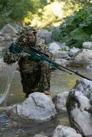 un' militare uomo o softair giocatore nel un' camuffare completo da uomo Sneaking il fiume e obiettivi a partire dal un' cecchino fucile per il lato o per obbiettivo. foto